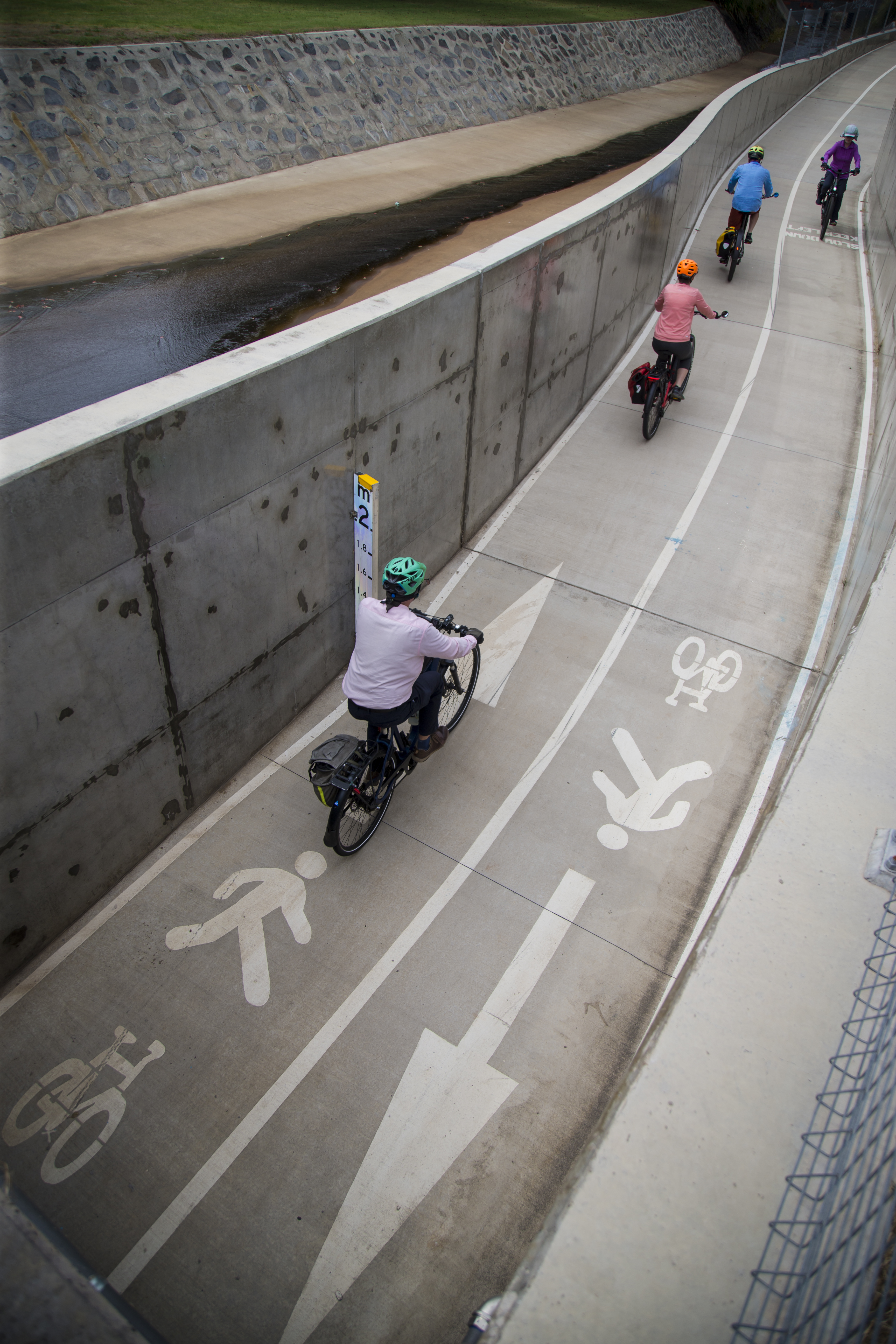 People on bikes come through a concentre underpass with pictures of arrows, stick figures and bicycle showing the direction and which side of the path they can go. 