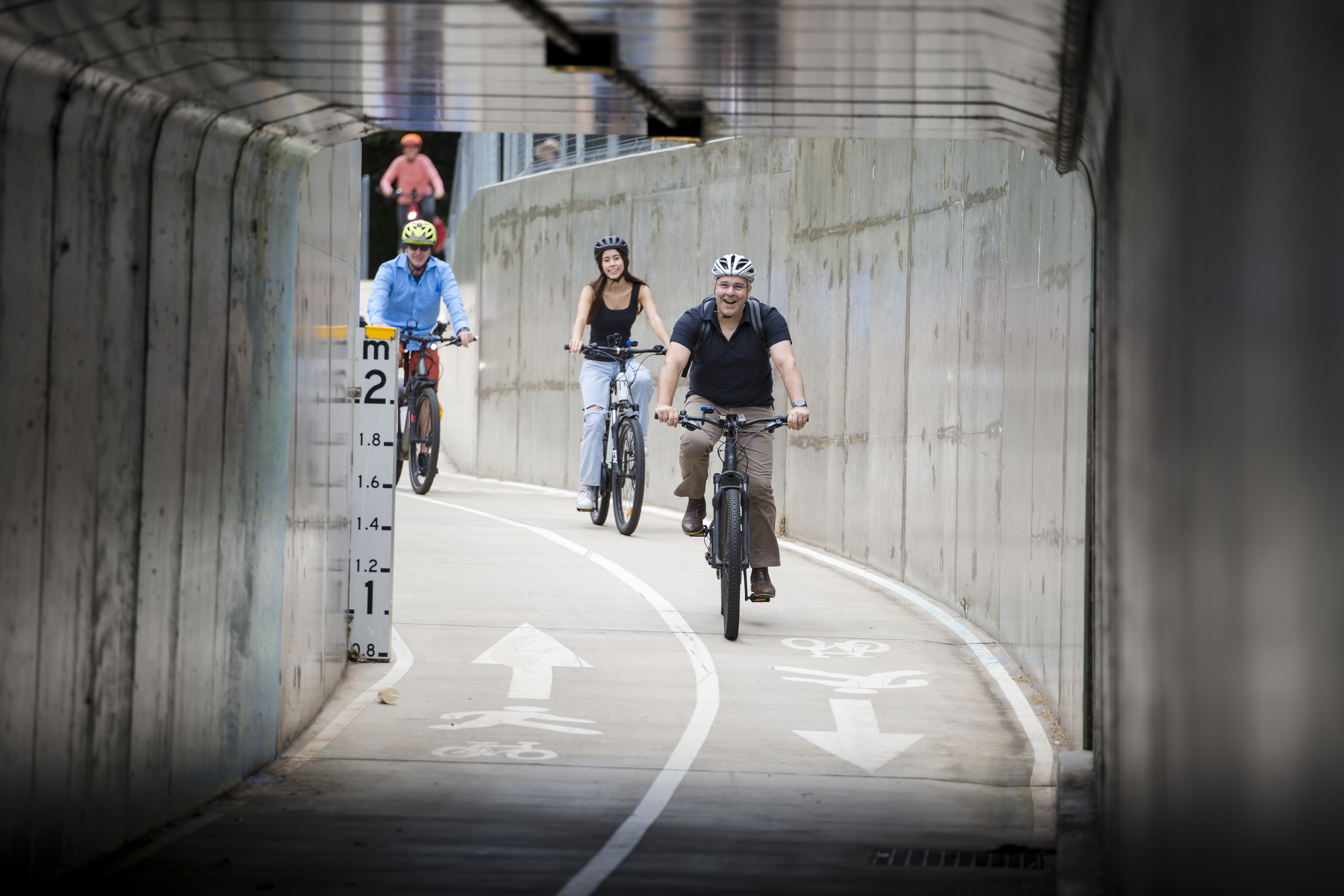 People riding bicycles who are about to go through the underpass concrete tunnel. 