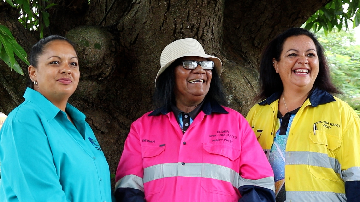 3 women in bright clothing in front of a tree