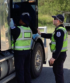 Two travel inspectors standing at open driver truck door talking to driver