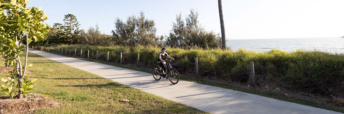 A person riding a bike along a path next to the ocean.