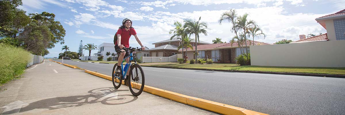A bike rider riding along a path running adjacent to a broad, straight residential street.