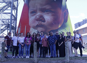 Group of people standing in front of a First Nation Australian person artwork.
