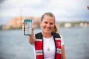 A woman with a large body of water behind her, holding a phone to the camera, showing the Digital Licence app.