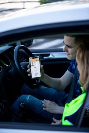 A man sitting in the driver seat of a car, showing his phone screen to a woman in the passenger seat.