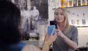 A woman behind a bar, using her phone to scan the phone of a customer who is showing her the phone screen.