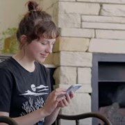 A woman sitting in a chair, looking at and typing on her phone. 