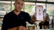 A person holding out a phone screen, with 'Show this QR code to share your details', their photo, a QR code, and a timer on the screen showing 9 seconds.