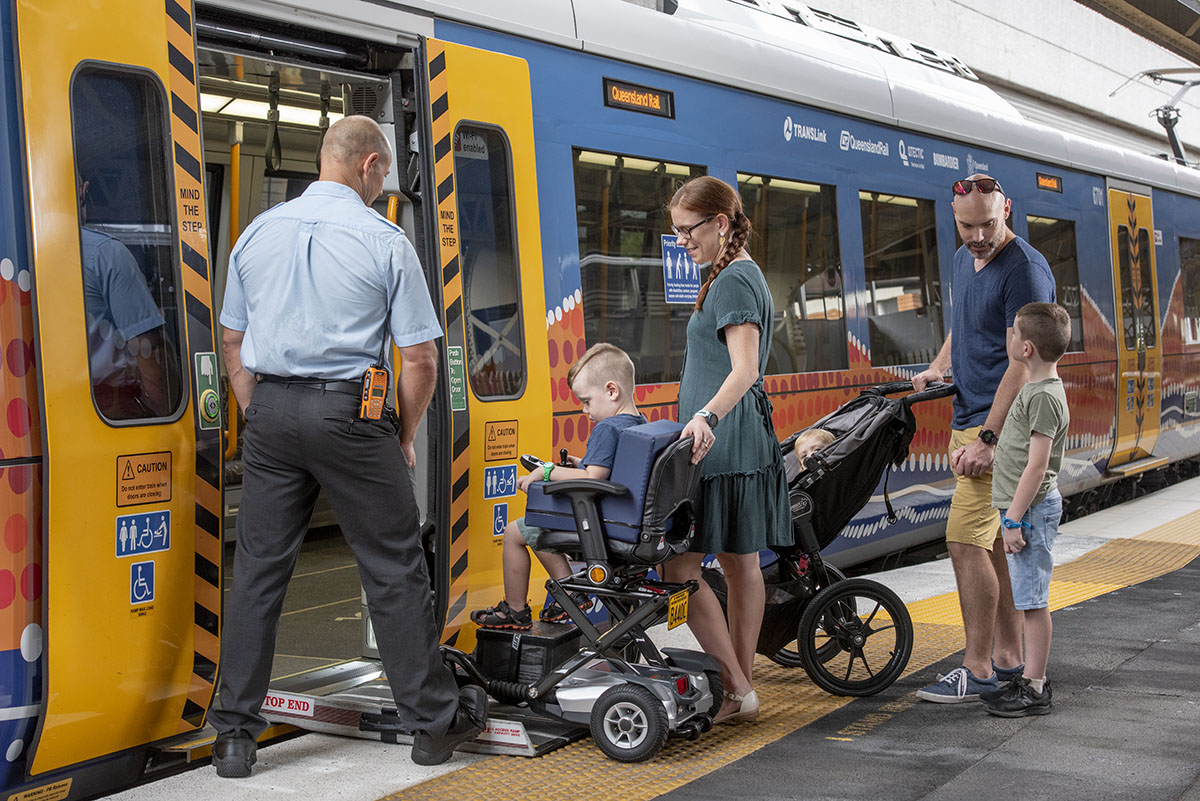 A family boarding a train. One child is in a wheelchair and another is in a pram