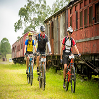 3 bicycle riders on trail, next to old train carriages