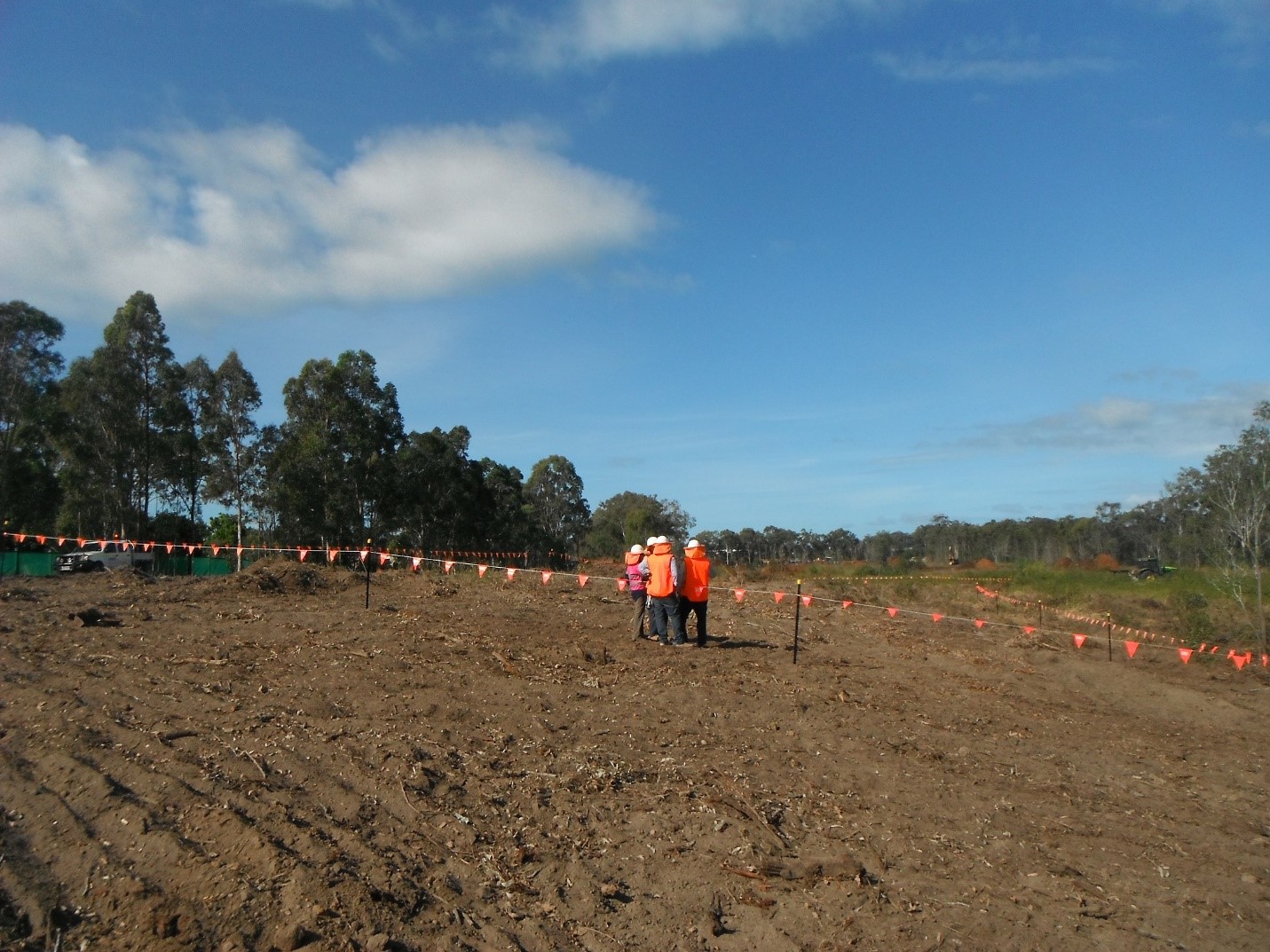 A dirt field with workers in the corner, surrounded by a flagged rope
