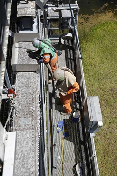 Abrasive blasting the surface of a downstream top chord (steel bridge deck)