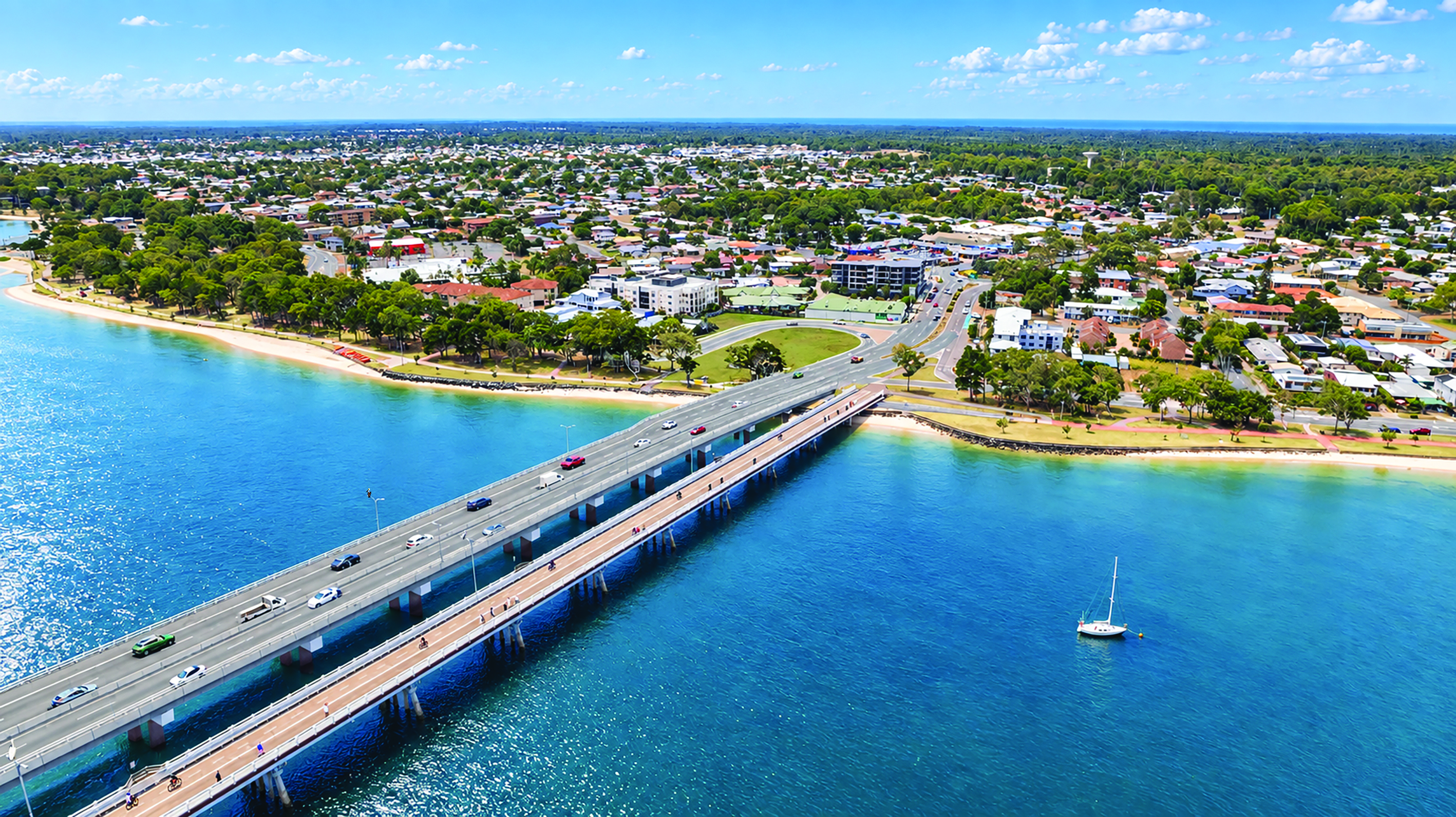 Aerial view of two bridges with motor cars on the left bridge and people on the right bridge over a channel with building, trees and sky in the background.