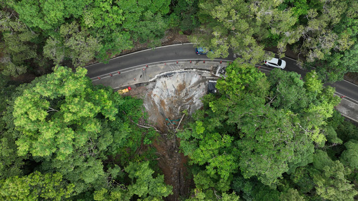 Kuranda Range Road, temporary stabilisation repairs following a major landslip on the side of the road. Aerial image of Kuranda Range Road, showing large green trees and a curved road which has temporary stabilisation repairs following a major landslip on the side of the road.