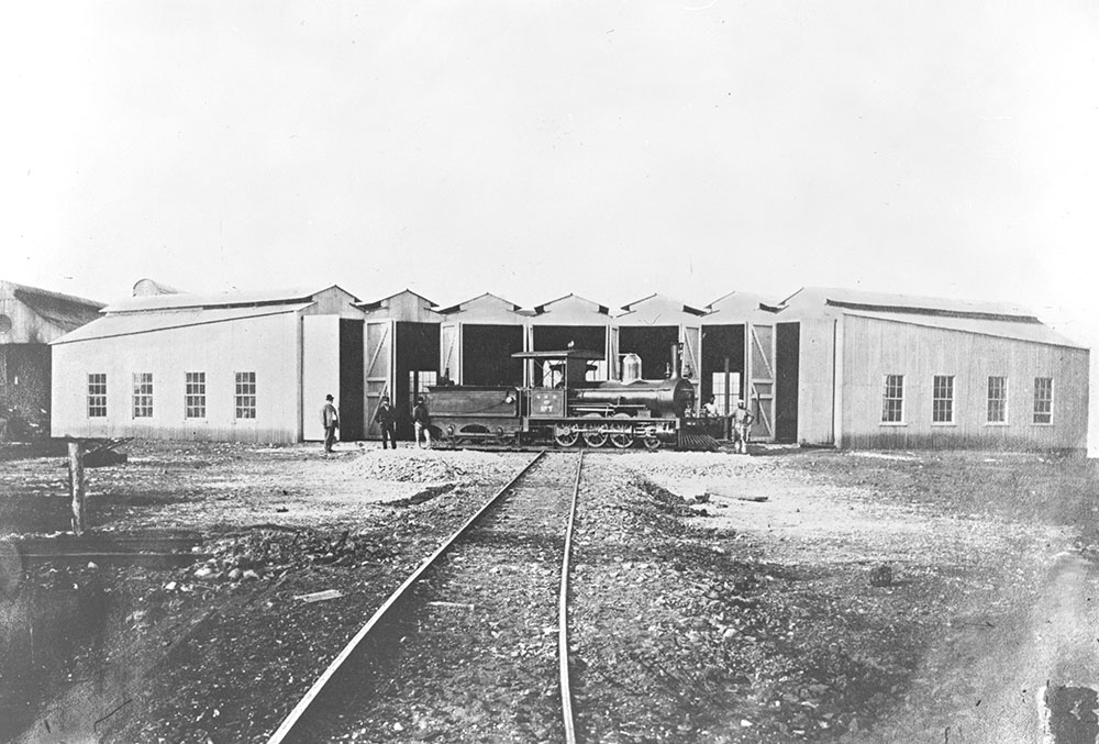 Historic black and white photograph of the completed partial Roundhouse in 1877, with rail tracks leading towards the structure