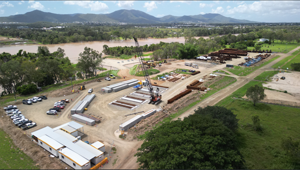 Rockhampton Ring Road new bridge location looking east across the Fitzroy River from Pink Lily where the exclusion zone will be in place. Foreground shows construction laydown area with bridge construction materials, site office and crane moving precast concrete deck units, mid-field shows Fitzroy River, and background shows Mount Archer.