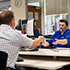 Man sitting at service centre desk, handing document to staff member sitting on other side of desk.