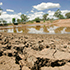 Drought-affected landscape with cracked dry soil, receding lake shoreline, and clear sky in the background