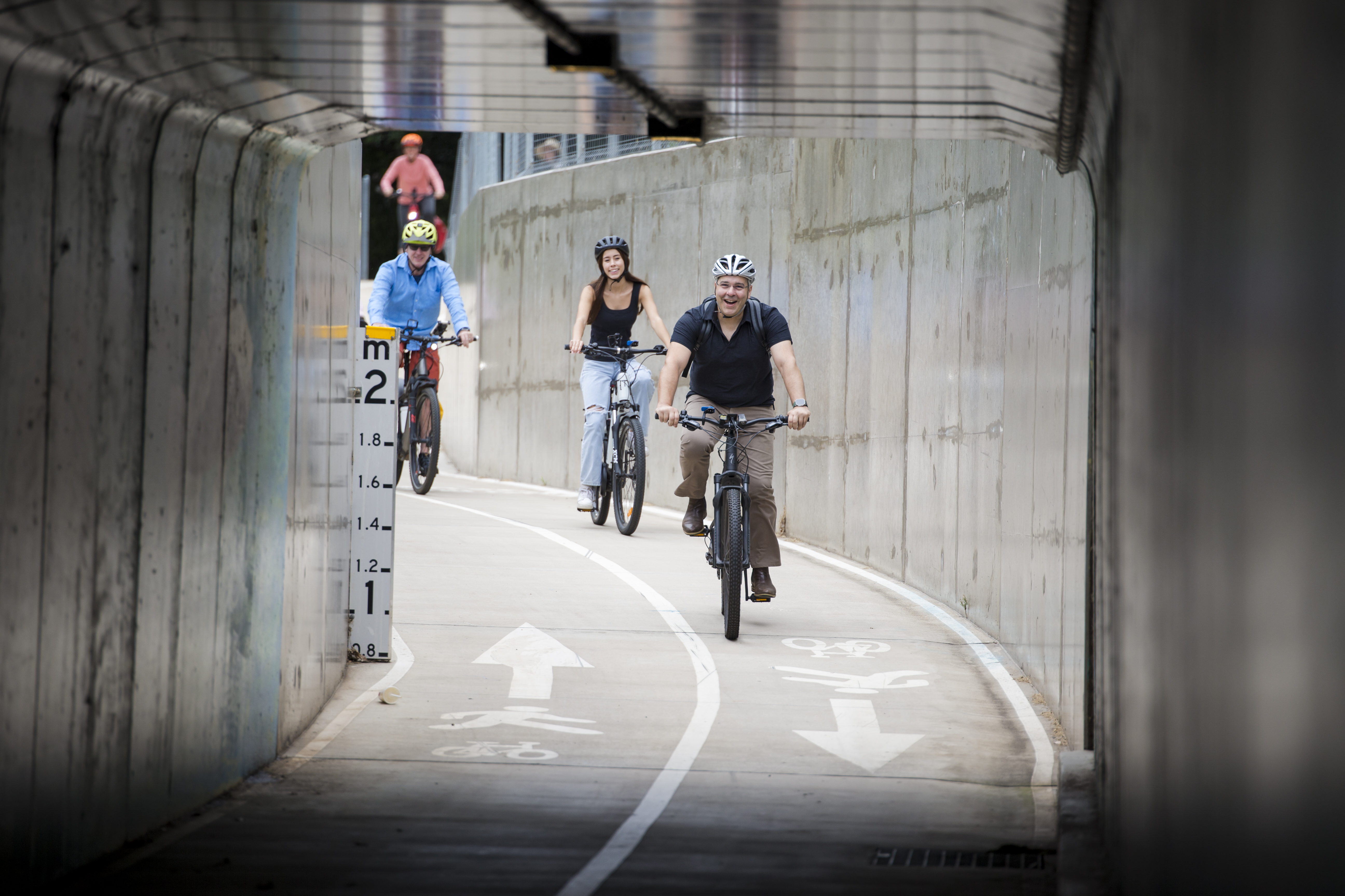 People riding bicycles who are about to go through the underpass concrete tunnel.