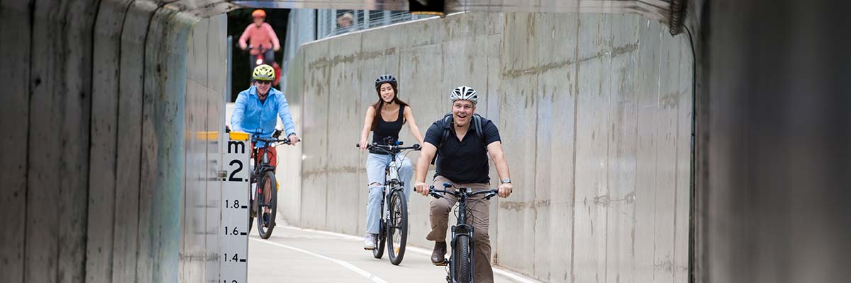 3 people riding bikes on a shared path. The path has concrete walls.