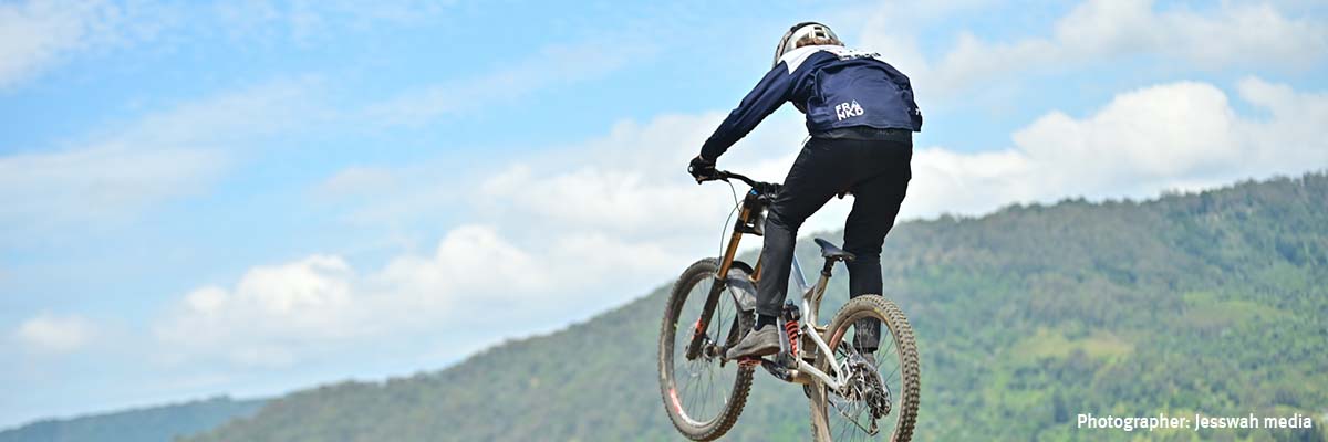 A person doing a jump on a bike, with mountains in the background. Small text in the bottom right corner says, "Photographer: Jesswah media".