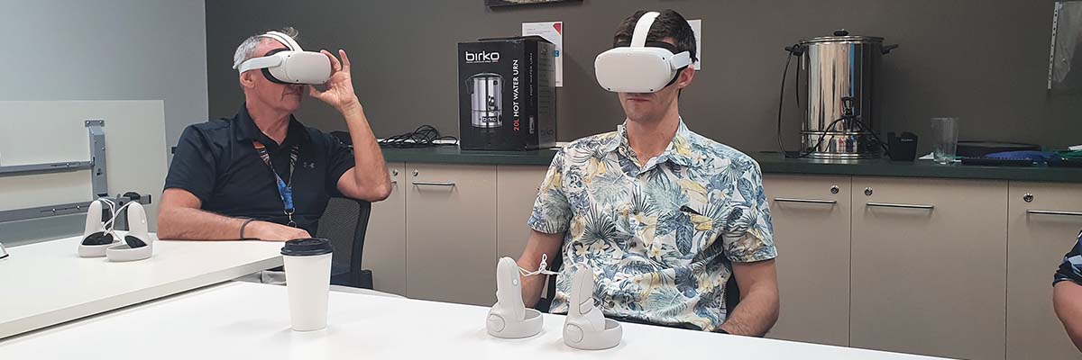 2 people sitting at a table wearing VR headsets