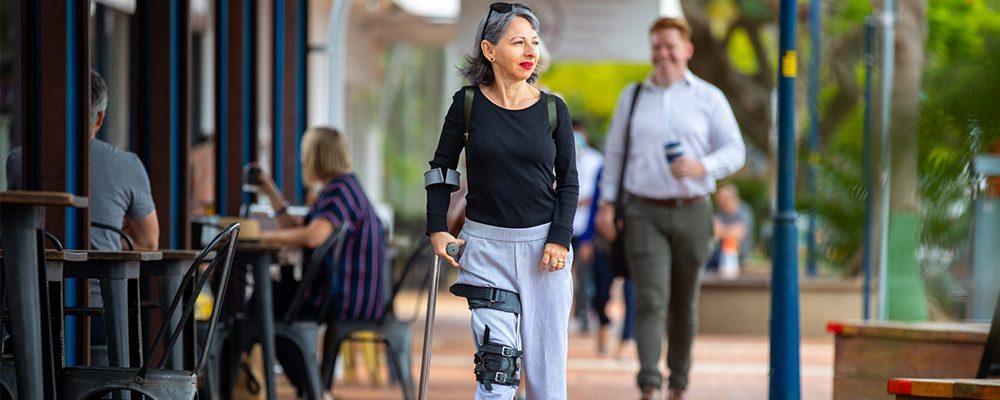 A person walking on a path next to a cafe with the help of a mobility device.