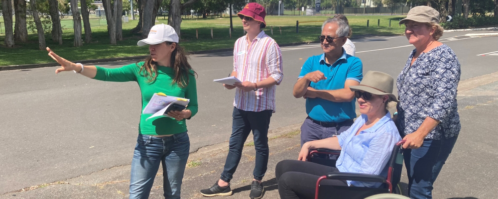 Six people on a footpath. One person in a wheelchair, other five standing. All looking towards something, suggesting that they are working on walking network plans. 