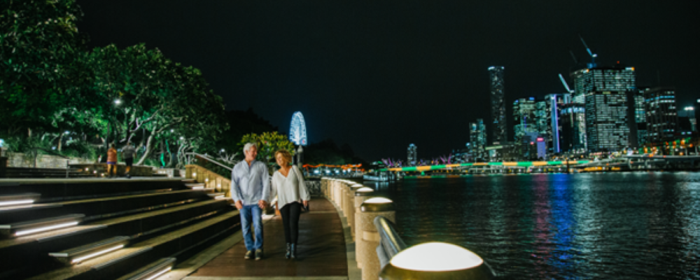Two people walking along a path next to a river, at night.