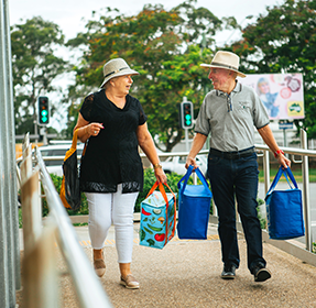 Older people walking on footpath carrying picnic bags
