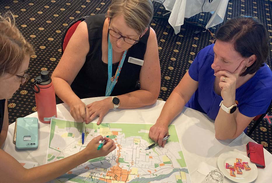 3 ladies sitting at a table looking and working on a map. 