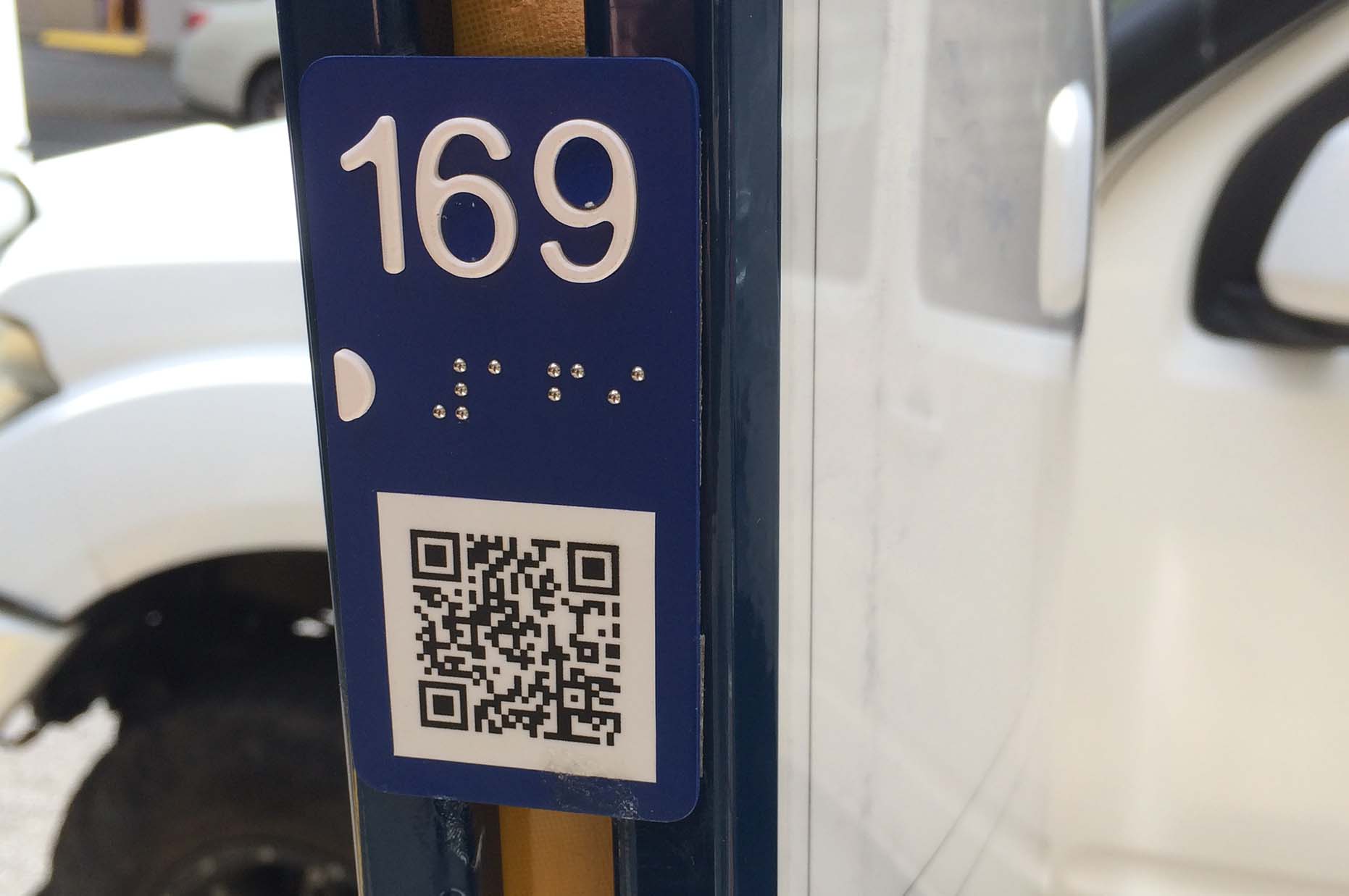 Bus stop with 169 written numbers and in braille, also displaying a QR code
